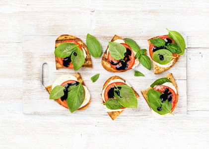 Caprese sandwiches with tomato mozzarella cheese basil and balsamic glaze on white painted wooden background