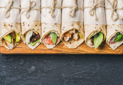Tortilla wraps with different fillings on dark grey concrete background