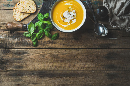 Pumpkin cream soup in bowl with fresh basil and spices