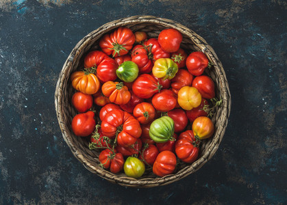 Fresh ripe Fall heirloom tomatoes in basket over plywood background