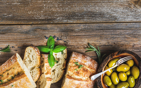 Green olives and slices of ciabatta over rustic wooden background