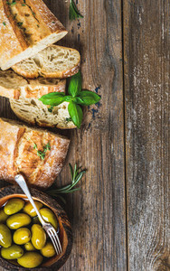 Green olives and slices of ciabatta over rustic wooden background