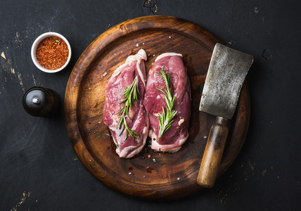 Raw duck breast with rosemary spices on dark wooden tray