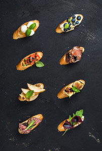 Italian crostini with various toppings on black plywood background
