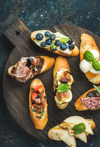 Italian crostini with various toppings on round wooden serving board