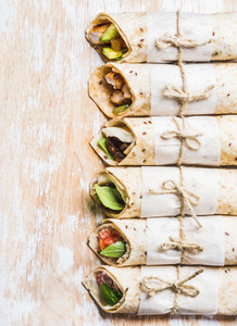 Tortilla wraps with various fillings on shabby white wooden board