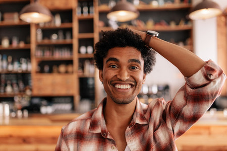 Young man smiling in a cafe with hand on head