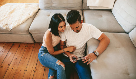 Young couple sitting together on floor with mobile phone