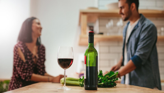 Wine on kitchen counter with couple cooking in background