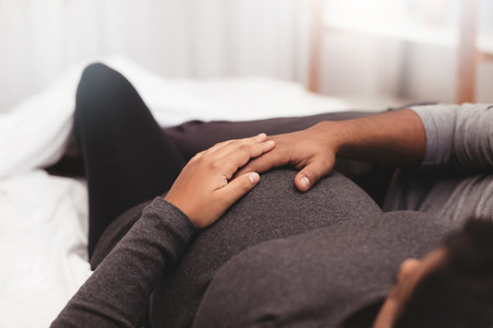 Pregnant couple with hands on belly lying on bed