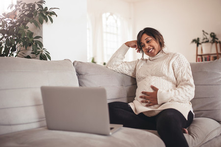 Happy pregnant woman on sofa using laptop