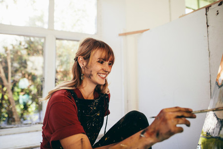 Female artist painting on canvas and smiling