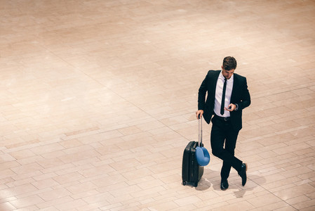 Businessman at airport terminal with suitcase and mobile phone