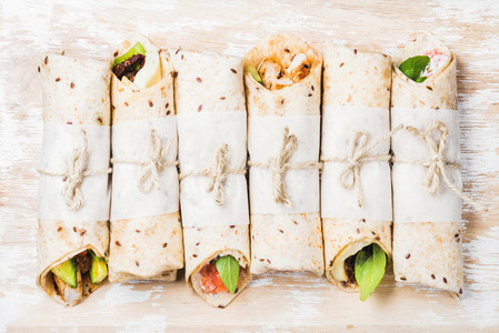 Tortilla wraps with various fillings on shabby white wooden background