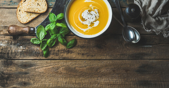 Pumpkin cream soup in bowl with fresh basil and spices