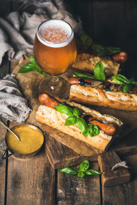 Glass of wheat beer and grilled sausage dogs in baguette