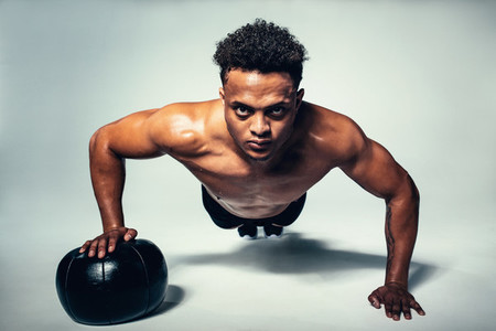 Muscular young man doing push up on medicine ball