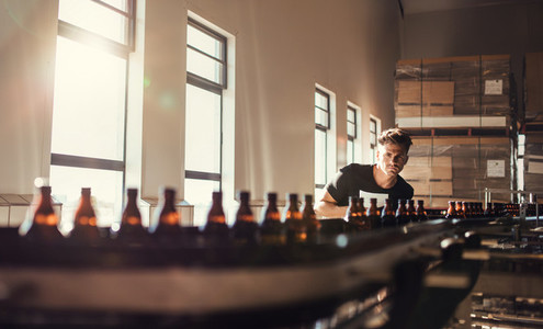 Brewer looking at conveyor with beer bottles