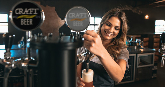 Female bartender tapping craft beer in bar