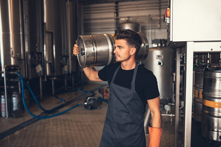 Young male brewer carrying keg at brewery