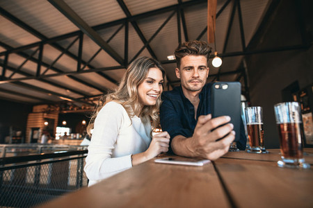 Young couple at the bar taking selfie with mobile phone