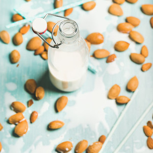 Dairy alternative almond milk in glass bottle over blue background