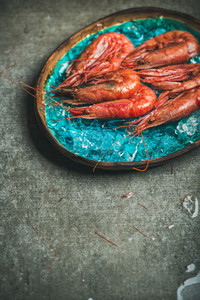 Raw uncooked red shrimps on ice in turquoise ceramic tray