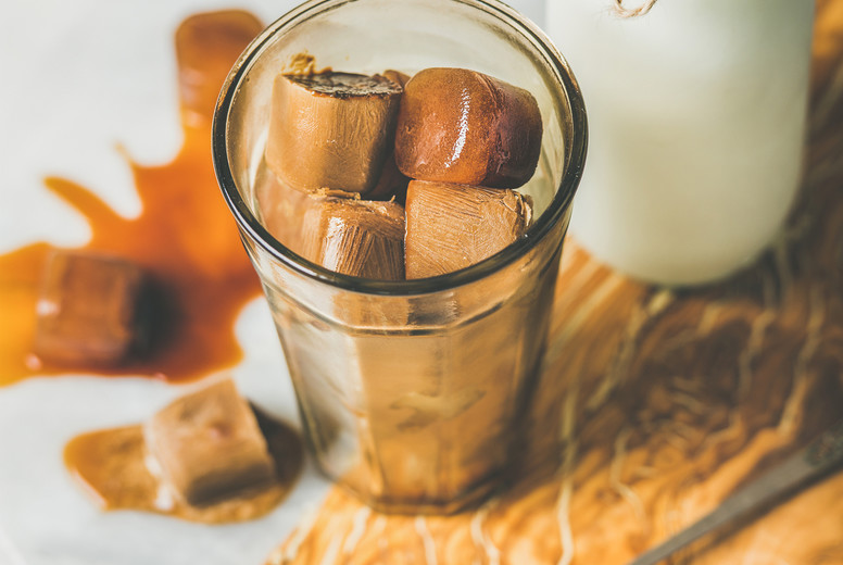 Glass with frozen coffee ice cubes and milk on board