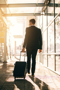 Young businessman walking with suitcase outside airport building