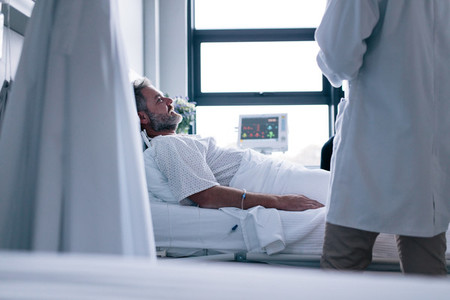 Sick man lying in hospital bed with doctor