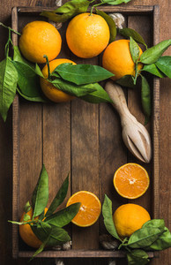 Fresh oranges with leaves in dark wooden tray over rustic background  copy space
