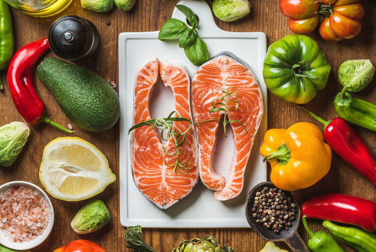 Dinner cooking ingredients. Raw uncooked salmon with vegetables, rice, herbs, lemon, artichokes, spices and bottle of rose wine on white ceramic board over rustic wooden background, top view