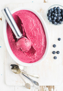 Homemade bluberry ice cream and scooper in mold served with fresh berries  silver spoons on white rusric wooden background