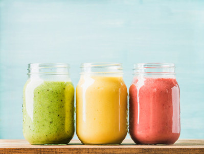 Fresh blended fruit smoothies of various colors and tastes in glass jars  Green  yellow  red