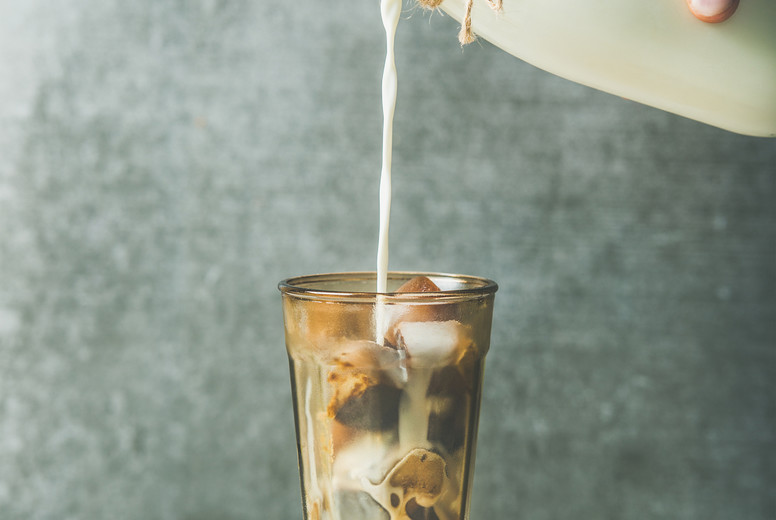 Man's hand pouring milk from bottle to glass with coffee