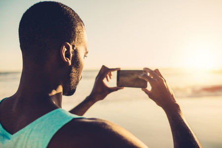 African man doing mobile photography on the beach