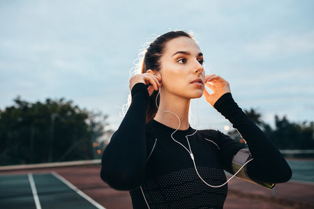 Beautiful young sportswoman with earphones on tennis court