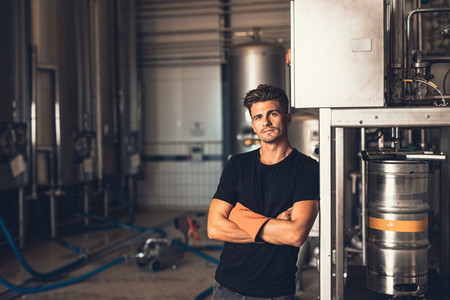 Young man standing by beer filling machine