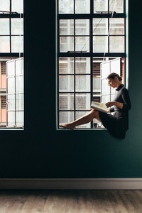Woman on window sill reading a magazine