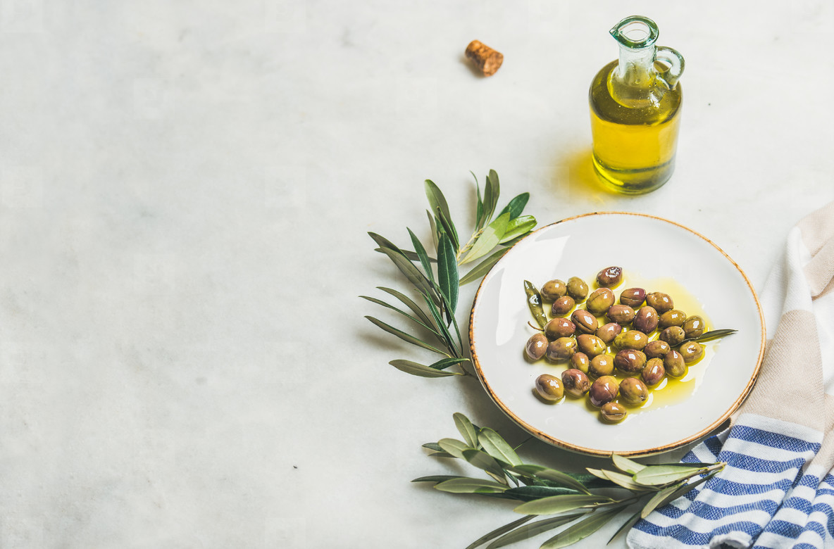 Pickled green Mediterranean olives, olive tree branch and oil