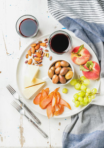 Wine snack set Cheese chicken carpaccio mediterranean olives fruits nuts and two glasses of red on ceramic plate over white painted wooden background