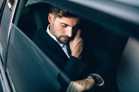 Businessman travelling by car checking time and talking on cellp