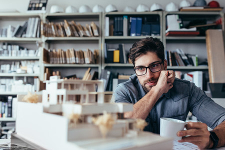Thoughtful male designer looking at model with cup of coffee