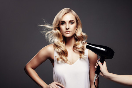 Gorgeous blond woman in a studio with hair dryer