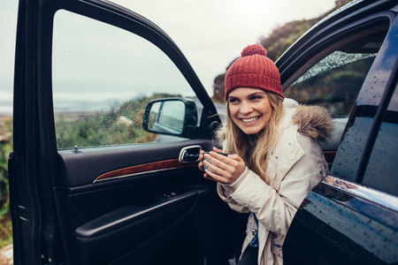 Beautiful smiling woman in her car drinking coffee
