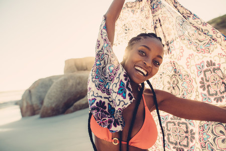 African woman holding scarf on the beach