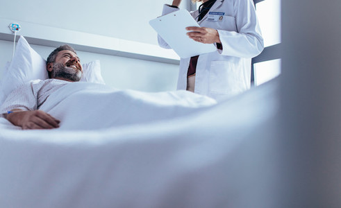 Smiling sick man lying with doctor standing by bed