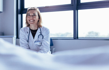 Happy female doctor sitting in hospital room