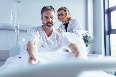 Doctor examining mature man in hospital bed