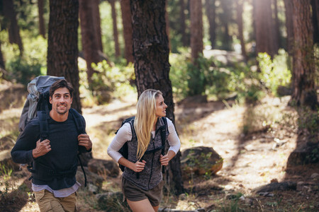 Hiking couple walking in forest wearing backpacks